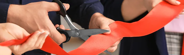 People holding a red ribbon and one cutting it with a scissor (Photo)