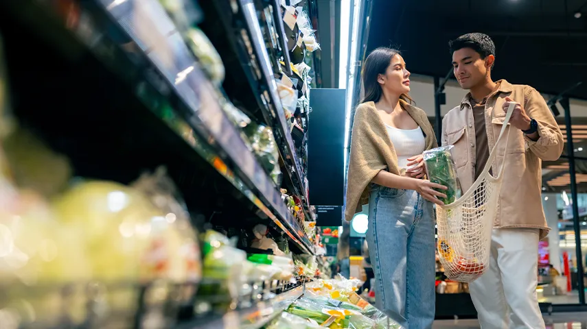 You've shared an image of two individuals shopping for food at a grocery store. The surroundings suggest a typical supermarket setting with various products on shelves and the presence of a cashier area.