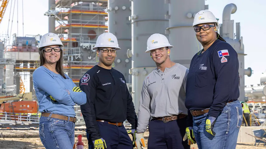 In the image, there are four people standing in front of a petroleum refinery. They are all wearing safety gear and jackets, indicating they may be part of a union or working crew.