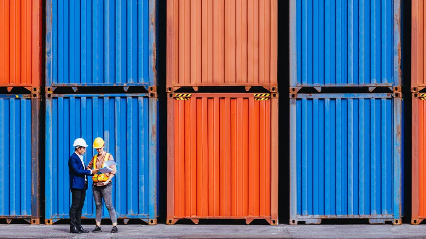 The image shows a person talking to another about a task involving large shipping containers.